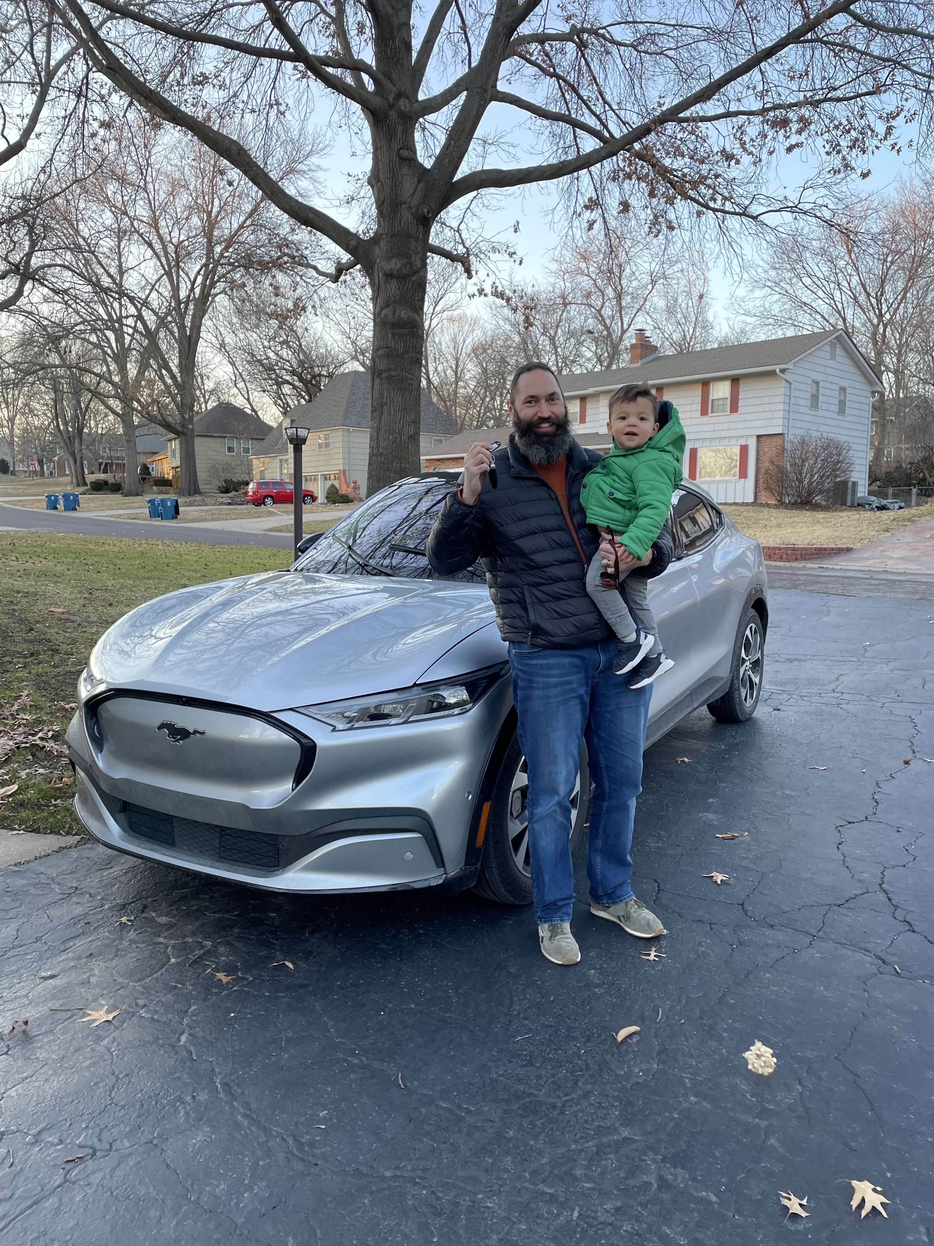 Clayton holding Oliver while posing in front of the Mustang Mach-E.